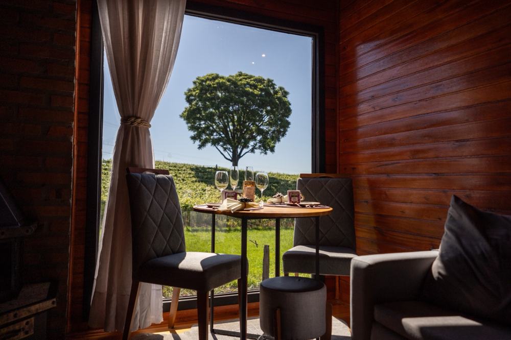 Mesa da Cabana Premium de frente pra janela com a árvore e o vinhedo
