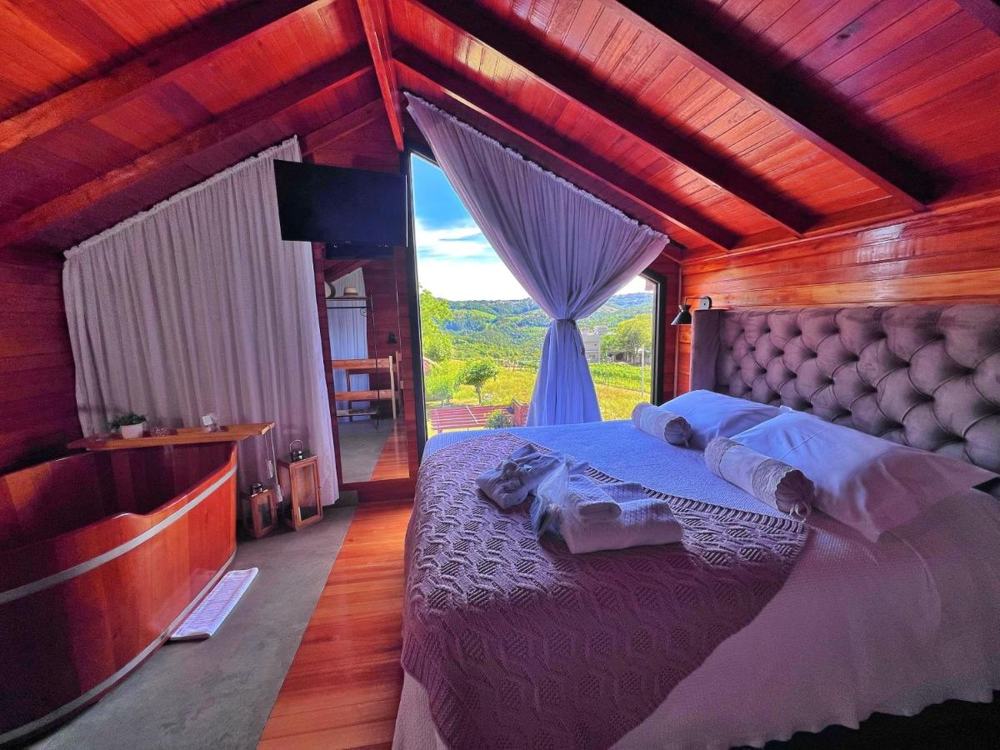 Quarto com a cama de casal e o ofurô de madeira ao lado da janela